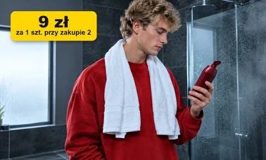 Młody mężczyzna z ręcznikiem na szyi ogląda butelkę żelu pod prysznic w łazience z ciemnymi płytkami