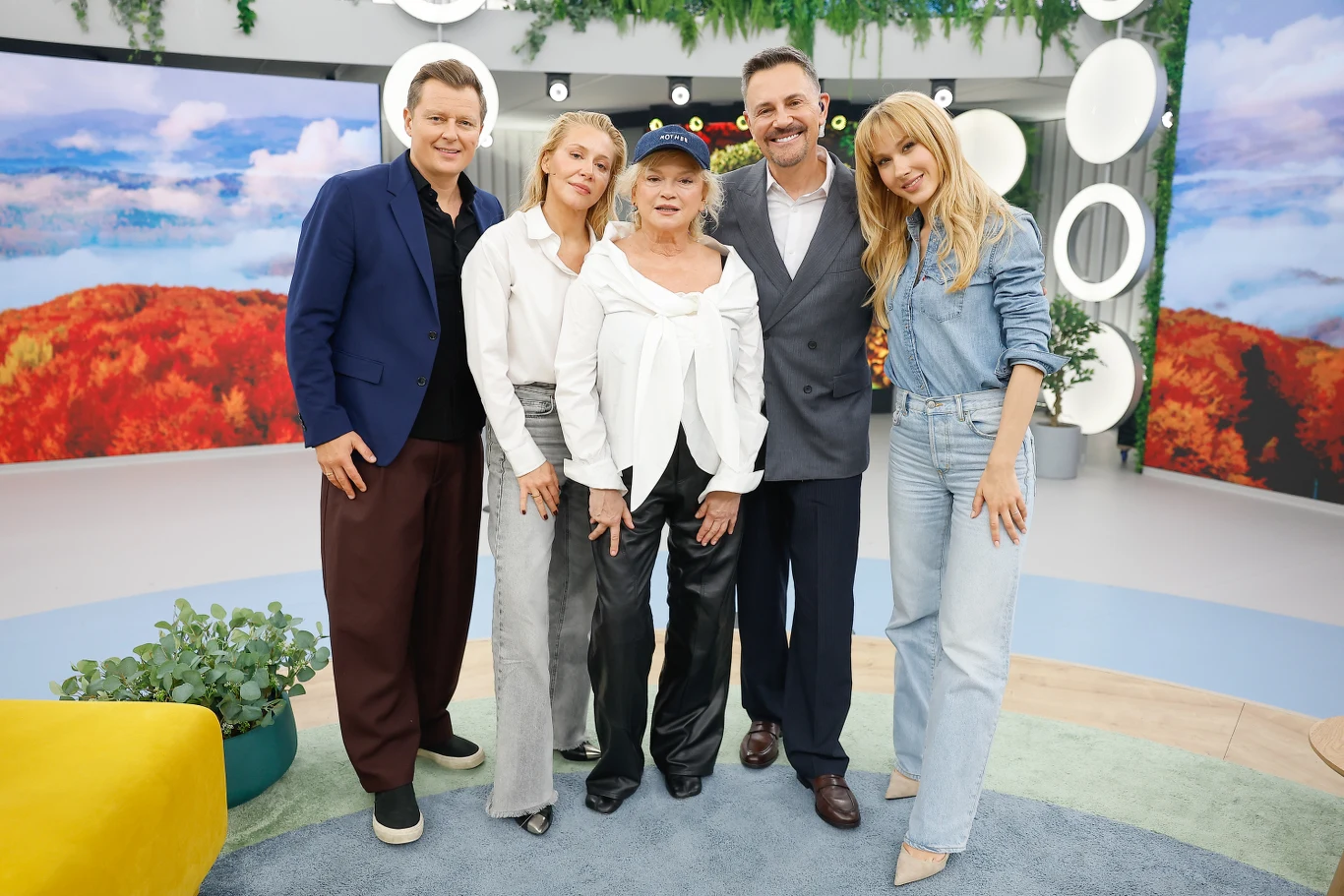 Rafał Brzozowski, Katarzyna Warnke, Katarzyna Figura, Krzysztof Ibisz, Ida Nowakowska w "halo tu polsat" Pięć uśmiechniętych osób pozuje razem w nowoczesnym, jasnym wnętrzu z kolorową, jesienną dekoracją w tle.