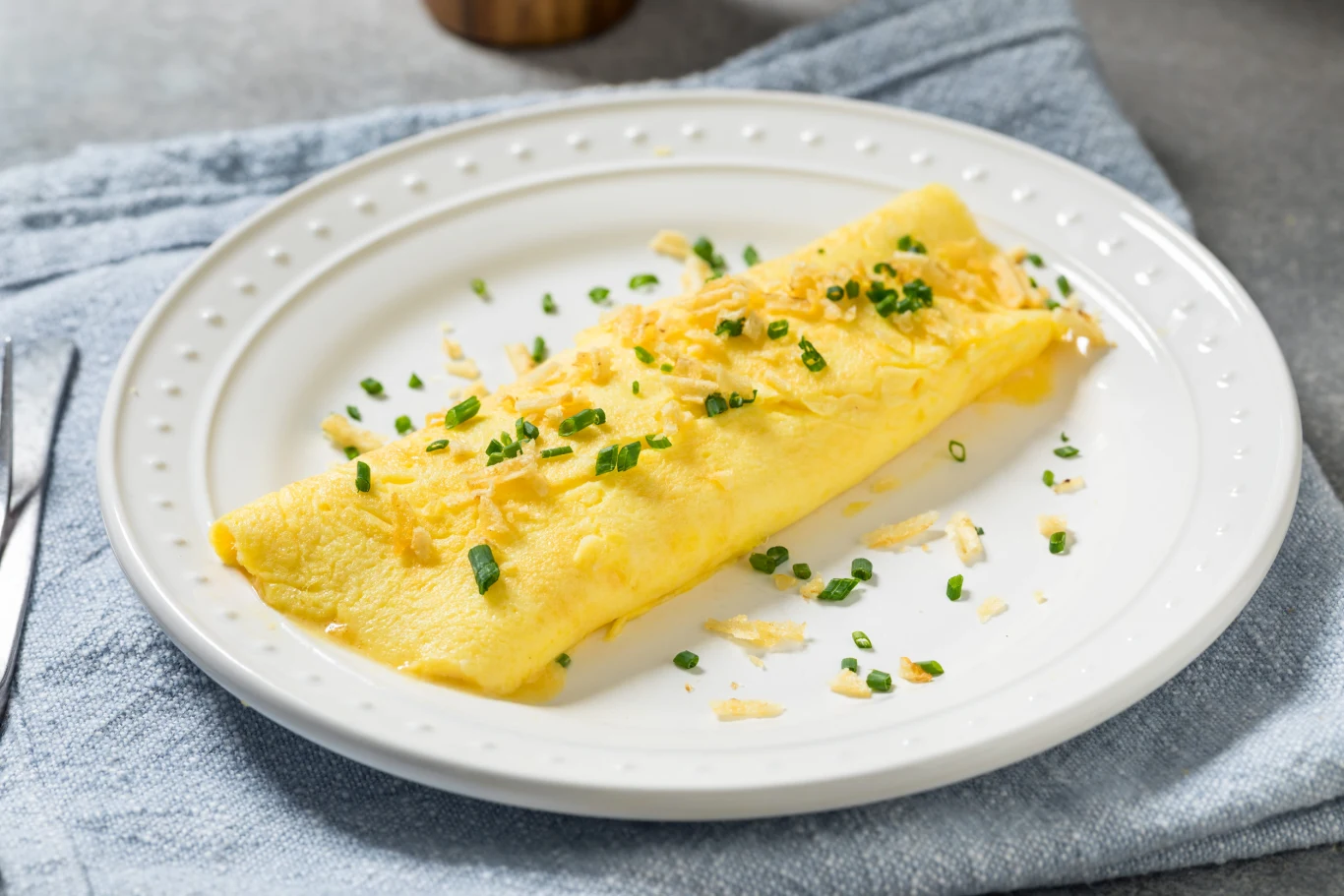 Francuski omlet to proste i sycące danie danie na pożywne śniadanie Francuski omlet posypany startym żółtym serem i szczypiorkiem na białym talerzu