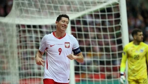 Piłkarz w biało-czerwonym stroju z numerem 9 i opaską kapitana na ramieniu podczas meczu, w tle bramkarz drużyny przeciwnej.