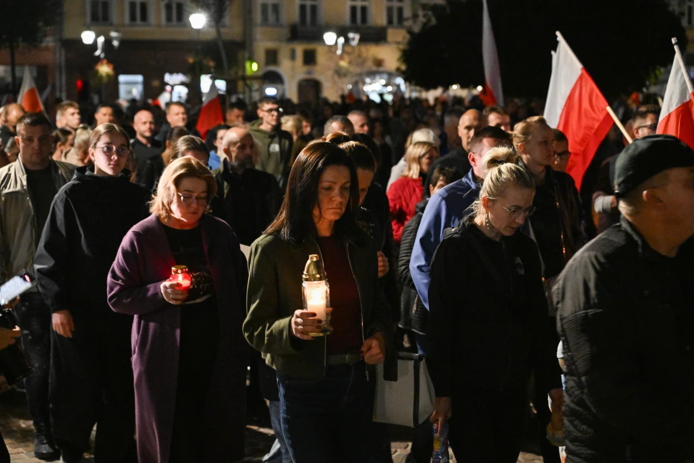 Marsz Ciszy w Jarosławiu Tłum ludzi idących razem wieczorem, niektóre osoby trzymają znicze, a w tle widoczne są biało-czerwone flagi.