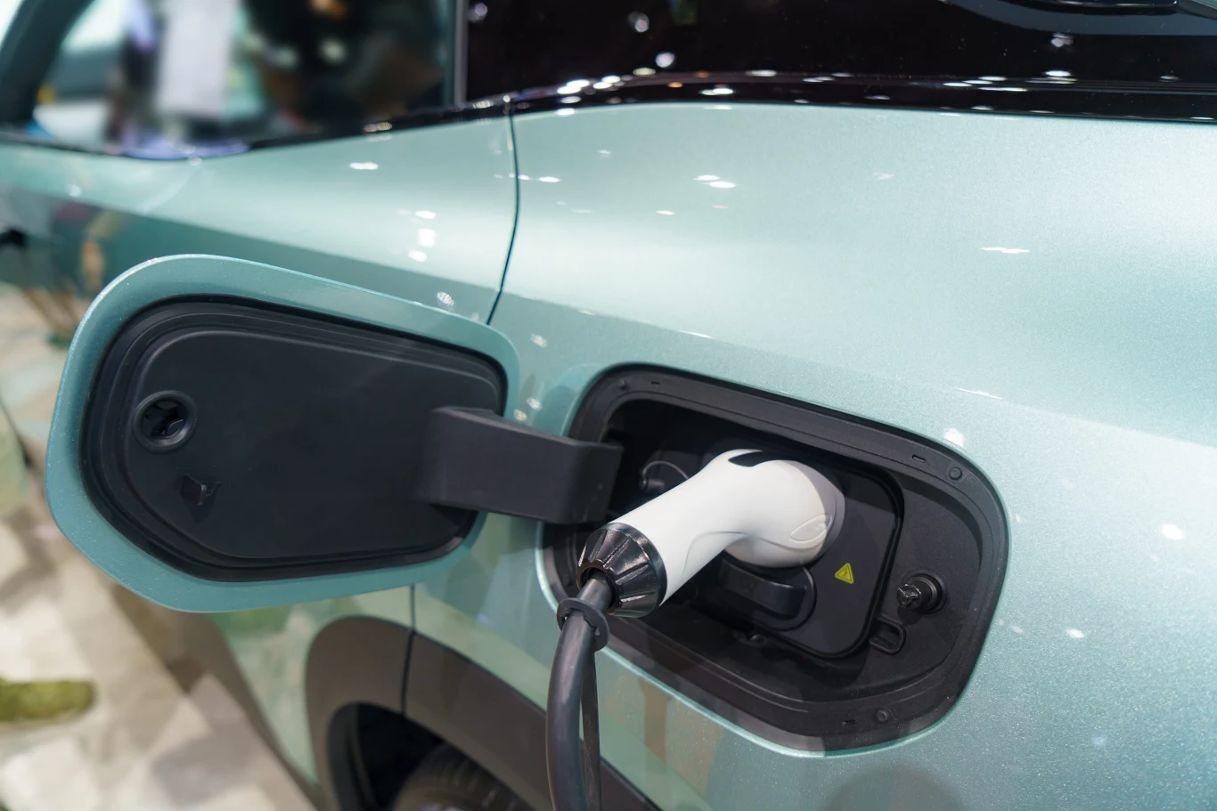 Biały przewód ładowania podłączony do portu w jasnozielonym samochodzie elektrycznym z otwartą pokrywą gniazda.