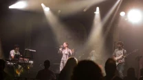 Zespół wykonuje utwór na scenie oświetlonej reflektorami, wokalistka śpiewa do mikrofonu, a pozostałych muzyków gra na keyboardzie, perkusji i gitarze elektrycznej; z przodu widoczne sylwetki publiczności.