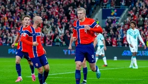 Piłkarze norweskiej drużyny narodowej w czerwonych koszulkach celebrują zdobycie bramki podczas meczu, na tle pełnych trybun stadionowych.