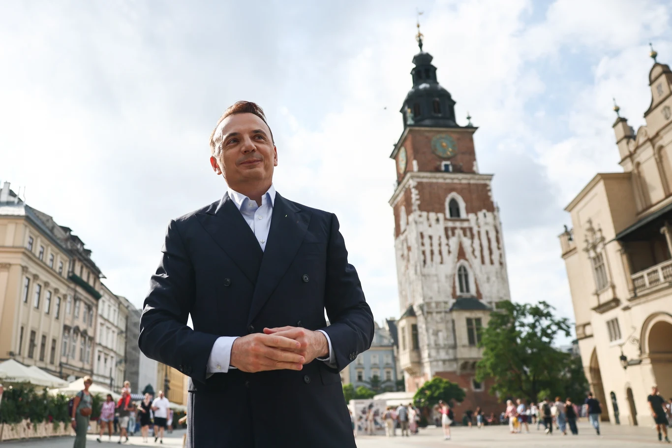 Kim jest Łukasz Gibała? Przedstawiamy jego sylwetkę Łukasz Gibała w garniturze na tle wieży kościoła Mariackiego na Rynku Głównym w Krakowie