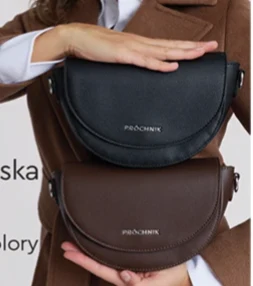 Torebka damska Dwie półokrągłe torebki w kolorze czarnym i brązowym z logo Procentik, trzymane przez osobę ubraną w brązowy płaszcz.