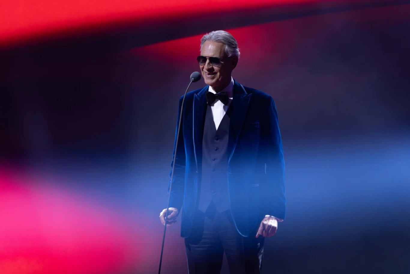 Andrea Bocelli wystąpi na Superauto.pl Stadionie Śląskim w Chorzowie Andrea Bocelli w ciemnych okularach śpiewa na scenie, czerwone i niebieskie światło.