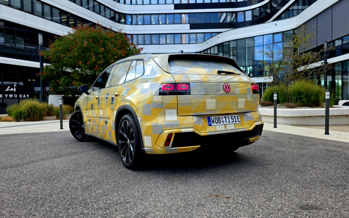 Kamuflażowy SUV marki Volkswagen na nowoczesnym dziedzińcu biurowym, z wyrazistym wzorem nadwozia i czarnymi felgami.
