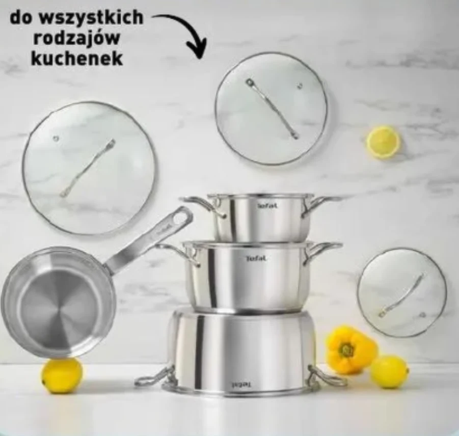 7-częściowy zestaw garnków Tefal Zestaw trzech stalowych garnków z pokrywkami, ułożonych jeden na drugim, obok nich patelnia z długą rączką oraz dekoracyjne cytryny i żółty kwiat na białym tle.