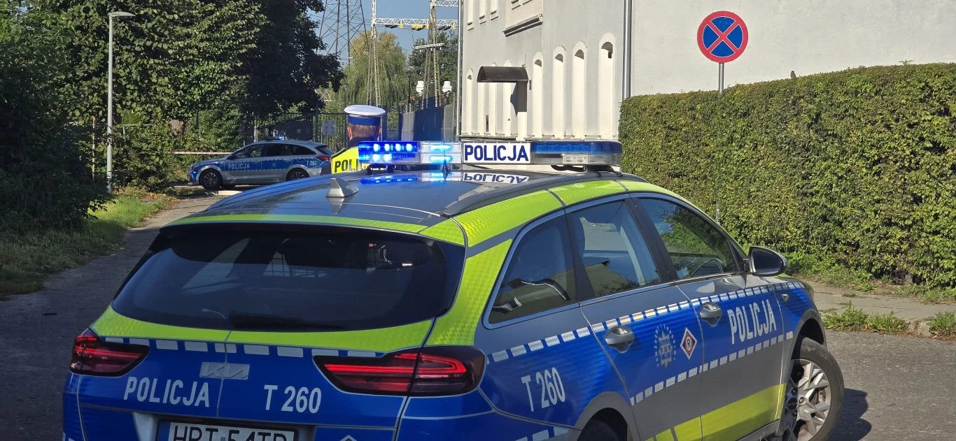 Radiowóz w pobliżu budynku w Elblągu, gdzie znaleziono butelki z nieznaną substancją Radiowóz policyjny z włączonymi sygnałami świetlnymi przed budynkiem w Elblągu, na ulicy przy znaku zakazu.