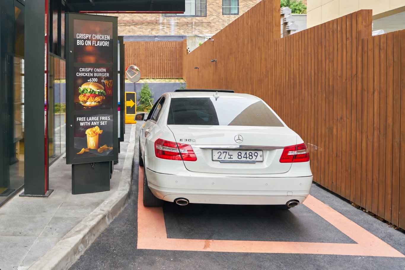 Mercedes zgłosił pomysł na zamawianie i płacenie w drive-thru przez ekran samochodu. Zdjęcie ilustracyjne. Biały Mercedes przy okienku drive-thru obok menu z kanapkami i frytkami w restauracji szybkiej obsługi.