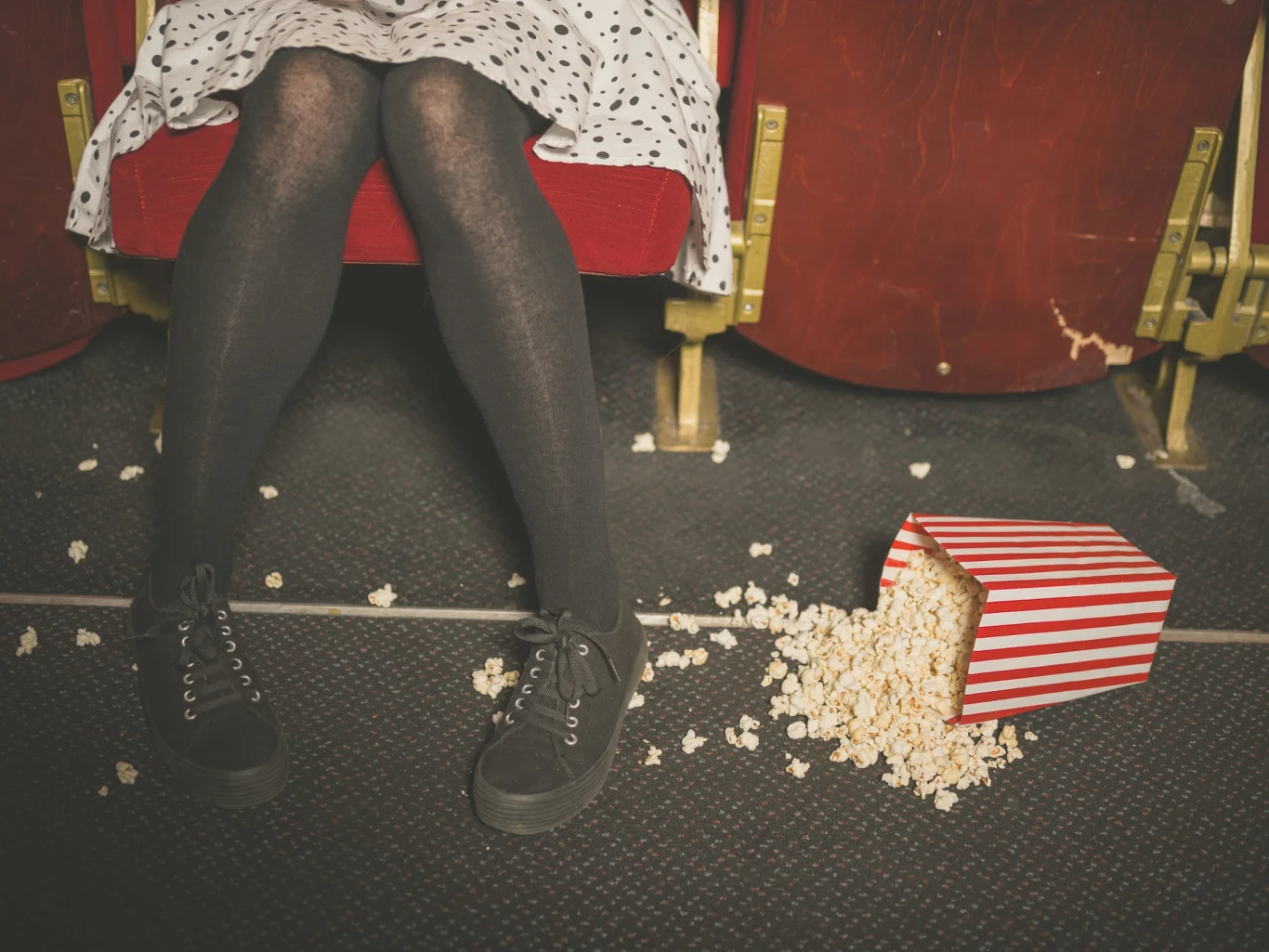 Rozsypany popcorn to codzienność. Ludzie po seansie zostawiają na sali przedziwne "pamiątki" Czerwone kinowe fotele, kobiece nogi w czarnych rajstopach oraz rozsypany popcorn z przewróconego, biało-czerwonego pudełka na podłodze.