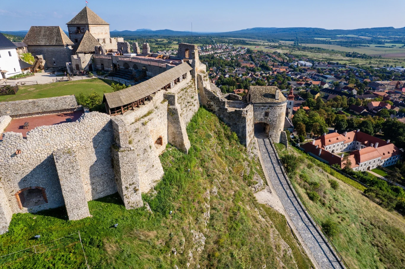 Węgry. Zamek Sümeg Kamienna twierdza z potężnymi murami obronnymi górująca nad rozległą panoramą miasteczka, otoczona zielonym wzgórzem.