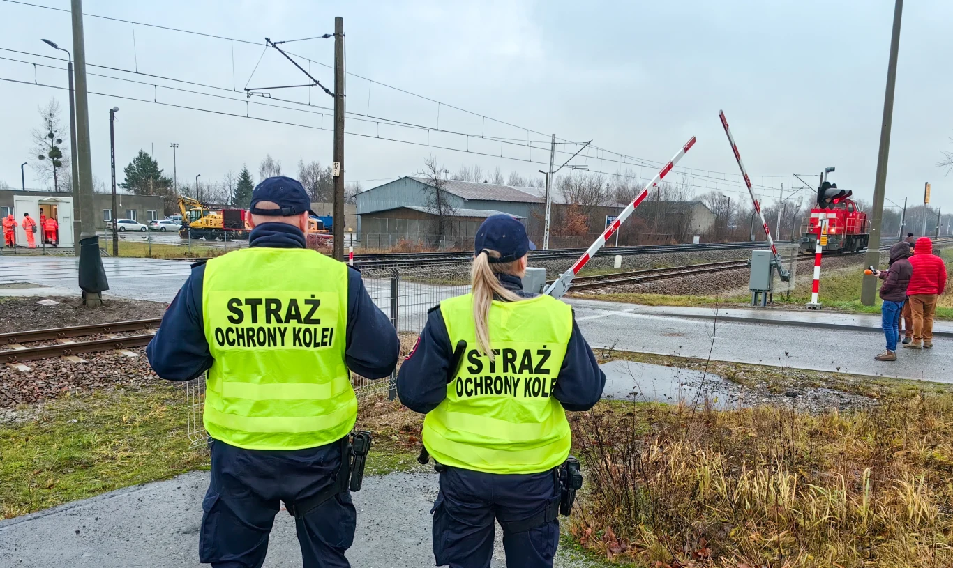 Na terenach kolei w Legnicy pojawiło się więcej mundurowych. To element międzynarodowej akcji. Dwóch funkcjonariuszy Straży Ochrony Kolei w kamizelkach odblaskowych przy przejeździe kolejowym, kontekst akcji w Legnicy.
