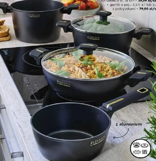 Garnki z pokrywkami Florina od 29,99 zł Czarny zestaw garnków i rondli z kolekcji Elegance ustawiony na nowoczesnej płycie indukcyjnej, jeden z naczyń wypełniony daniem z makaronem, warzywami i ziołami, a drugi przykryty pokrywką z widocznym brokułem w środku.