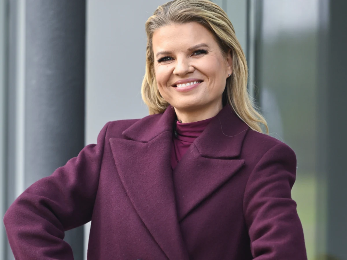 Marta Manowska Marta Manowska w fioletowym płaszczu i swetrze pozuje na tle nowoczesnego budynku ze szklaną elewacją.
