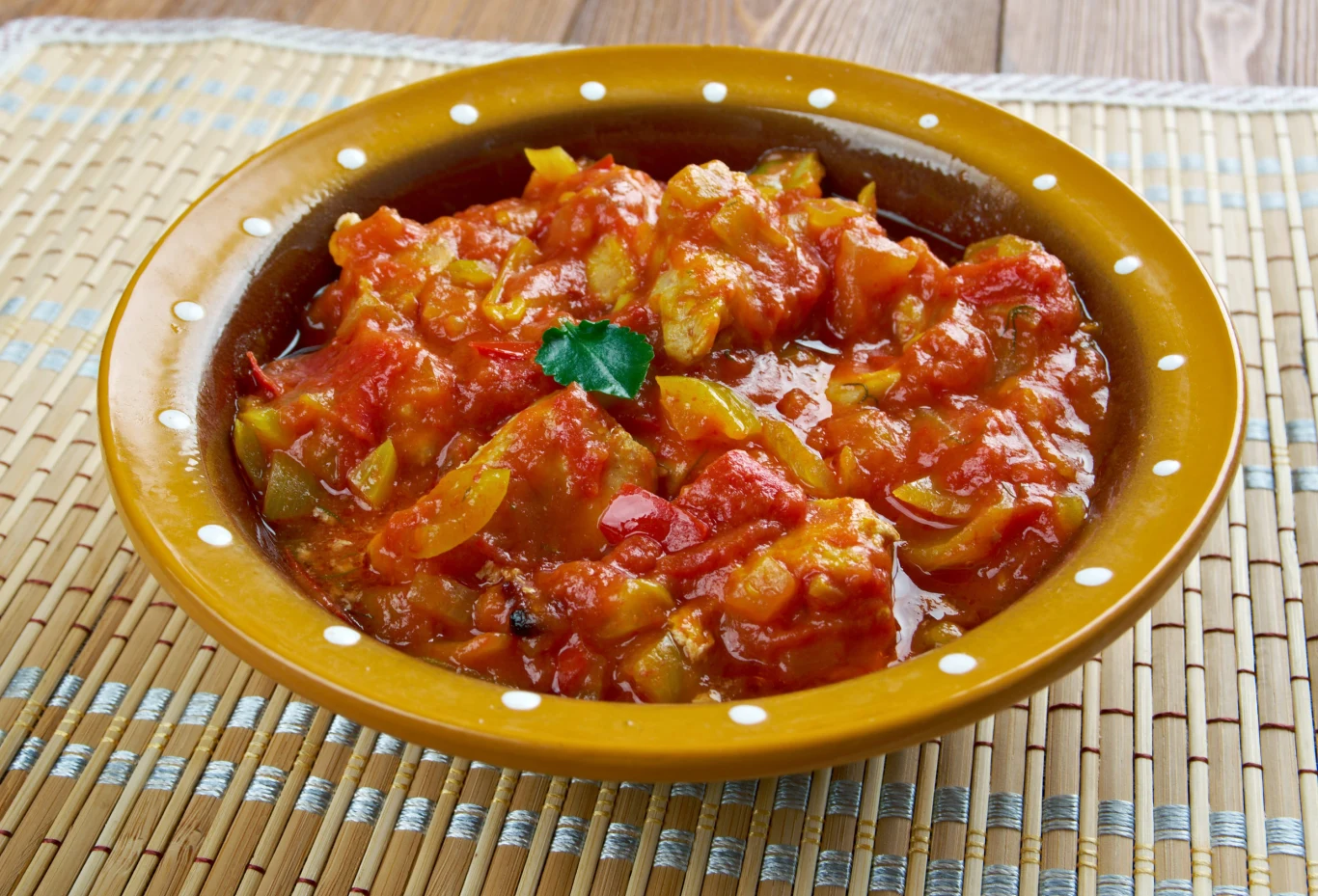 Gulasz z papryki pachnie i smakuje jak z dobrej restauracji. To zasługa wyjątkowego dodatku - wystarczy pół szklanki Gulasz z papryki, grzybów i pomidorów w żółtej misce z listkiem zioła, widoczne paski papryki i cebuli.