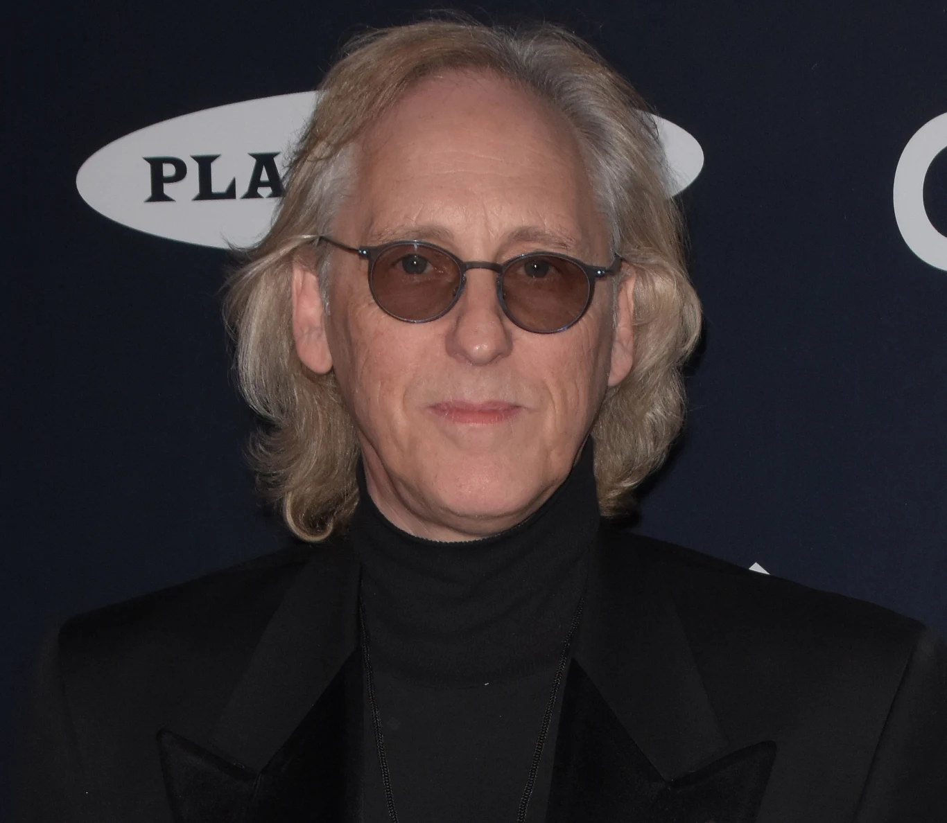 Eddie Jobson powróci do Polski pod szyldem Eddie Jobson's UK Revisited Eddie Jobson w czarnym garniturze i okularach przeciwsłonecznych na tle ściany z logotypami