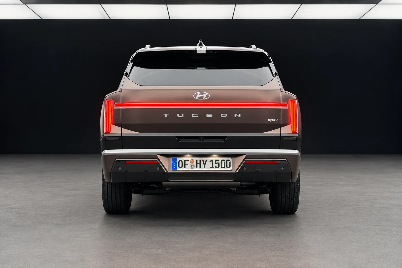Z tyłu pozioma listwa świetlna łączy się z pionowymi lampami. Napis TUCSON umieszczono pośrodku klapy. Tył samochodu Hyundai Tucson z charakterystycznym podświetlanym pasem LED biegnącym przez całą szerokość pojazdu, centralnie umieszczone logo marki oraz tablica rejestracyjna na dolnej części zderzaka.