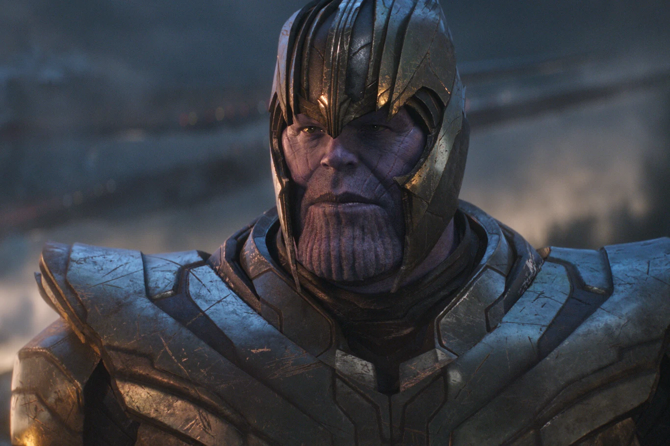 Kadr z filmu "Avengers: Koniec gry" Postać o fioletowej skórze w złoto-szarej zbroi i hełmie, stojąca na tle rozmytych struktur.