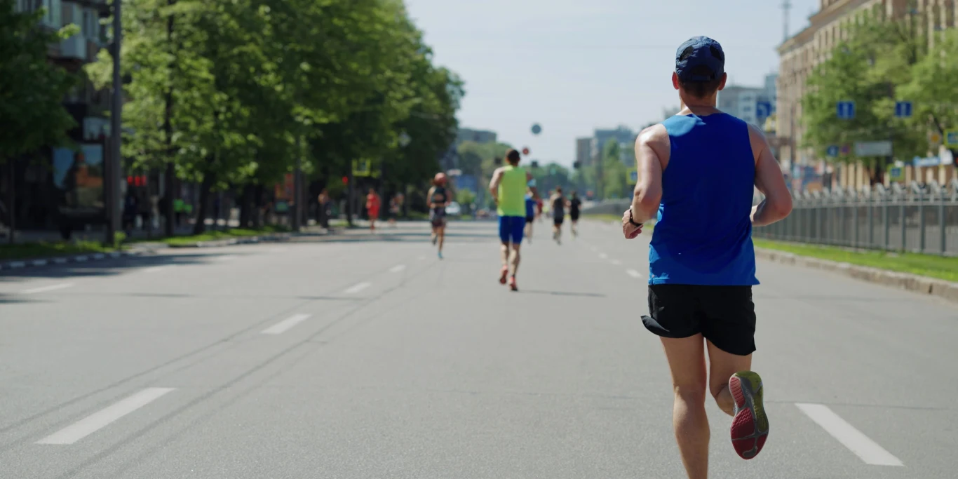 Półmaraton w Olsztynie. Jakie utrudnienia czekają mieszkańców miasta? Grupa biegaczy podczas półmaratonu na pustej, słonecznej ulicy Olsztyna w otoczeniu zieleni i zabudowy.