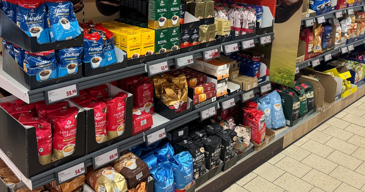 Dealz zaczyna październik mocną ofertą na Dzień Kawy. Markowe kawy już od 12 zł Półki sklepu z różnymi opakowaniami kaw znanych marek, widoczne ceny.