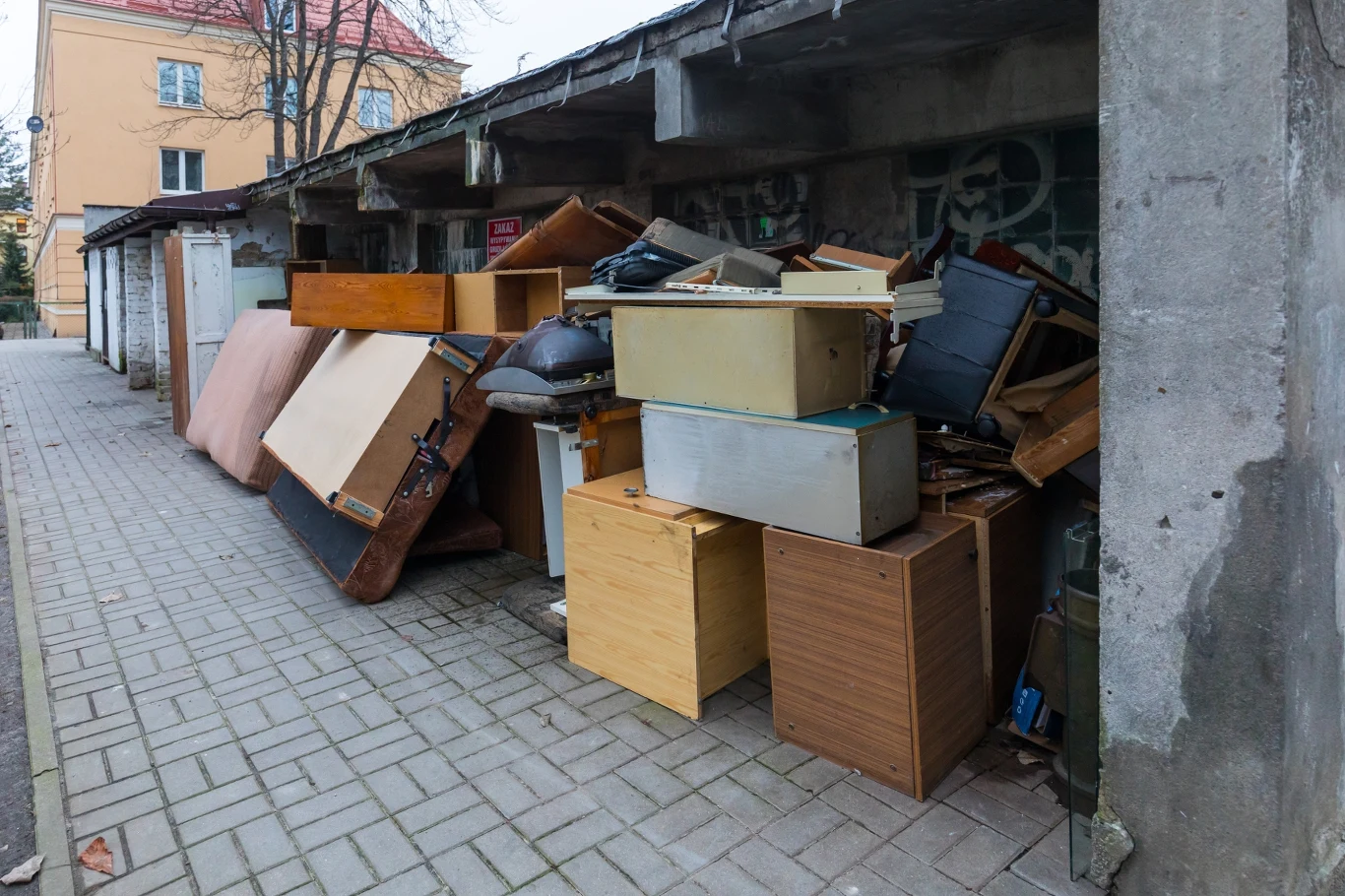Legnica organizuje zbiórkę odpadów wielkogabarytowych. Jak z niej skorzystać? Stare meble, materace i elementy wyposażenia wnętrz ułożone w stosie przy garażach na osiedlu, kontekst zbiórki w Legnicy