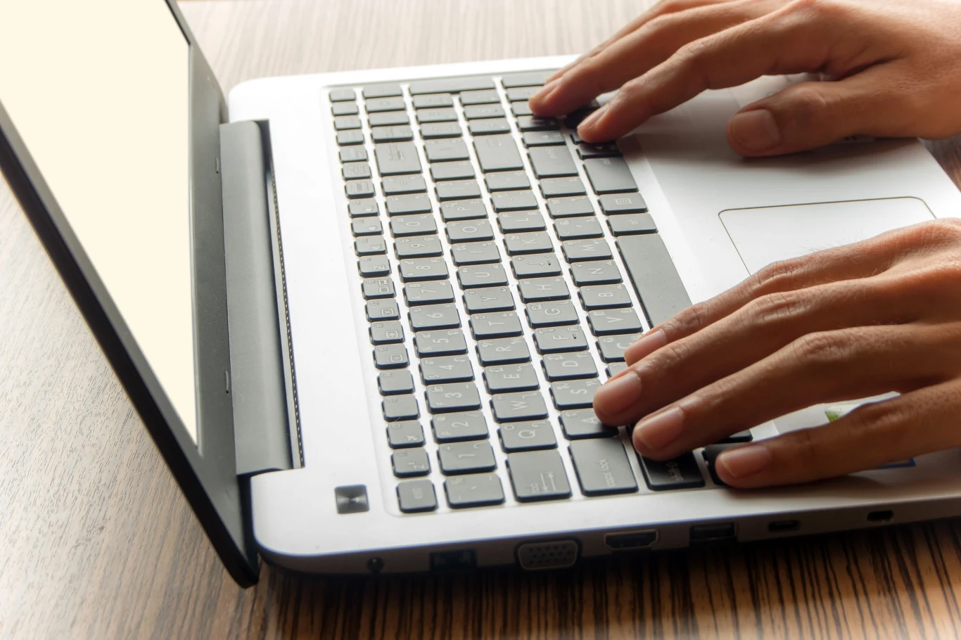 Od dzisiaj firmy muszą posiadać skrzynkę e-Doręczeń. CERT uspokaja, że wymóg nie jest wykorzystywany przez cyberprzestępców Dłonie piszące na klawiaturze laptopa na drewnianym blacie, ilustracja do tematu e-Doręczeń dla firm.