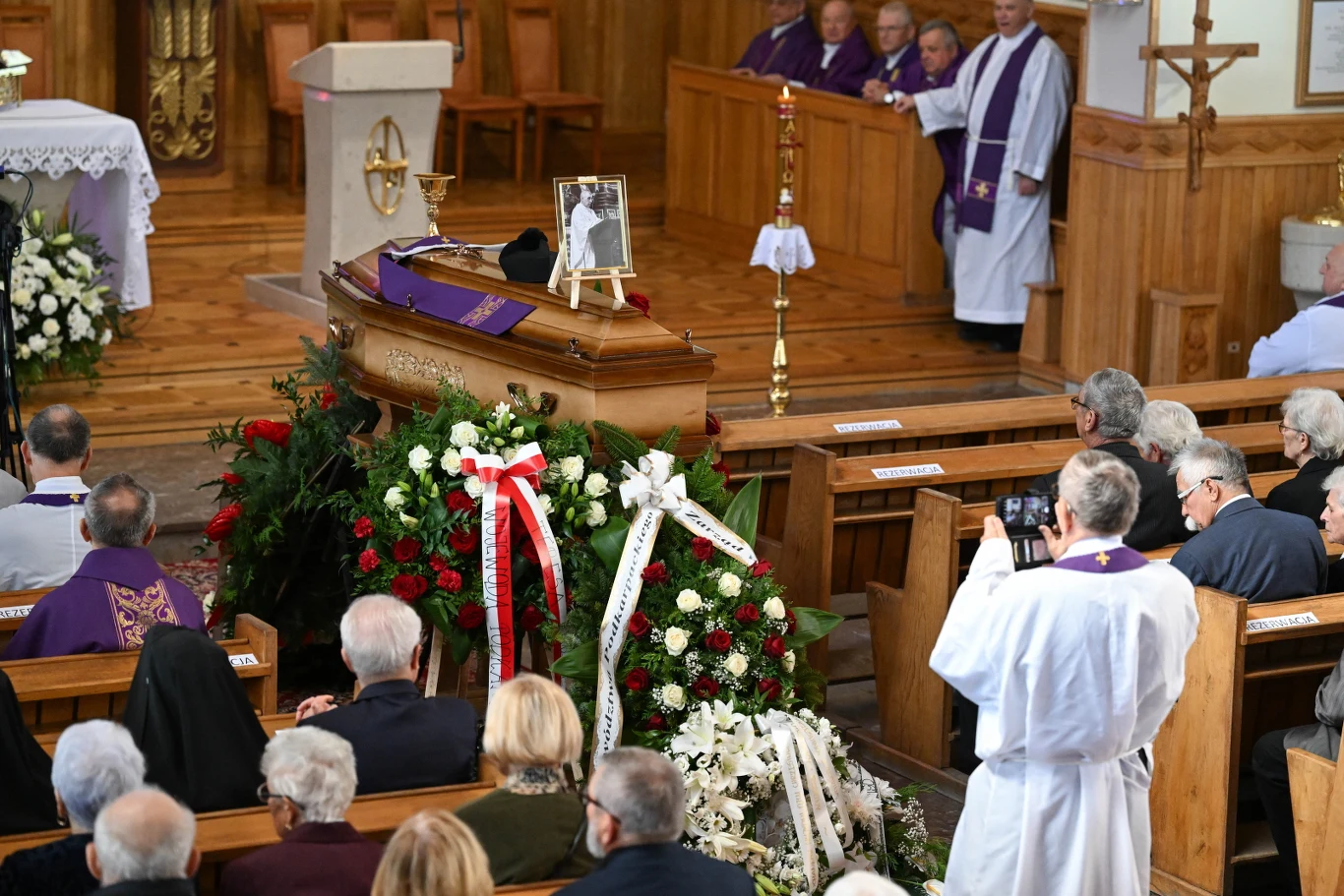 Ujawniono zeszyt po pogrzebie księdza Stanisława Zbojnowicza Trumna z portretem zmarłego, wieńce i kwiaty, żałobnicy w ławkach, duchowni przy ołtarzu podczas ceremonii.