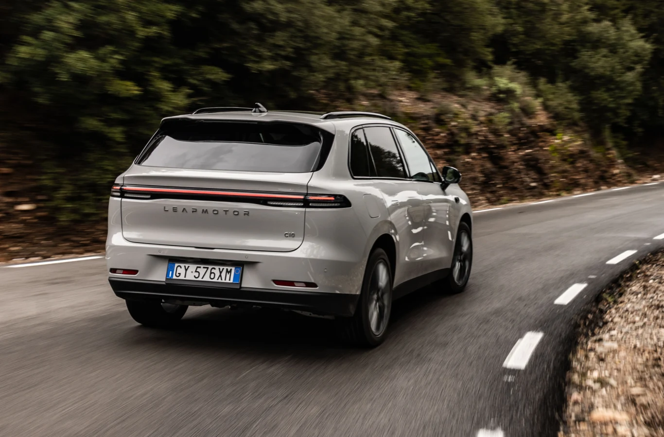 Biały SUV marki Leapmotor poruszający się po krętej, asfaltowej drodze otoczonej zielenią.