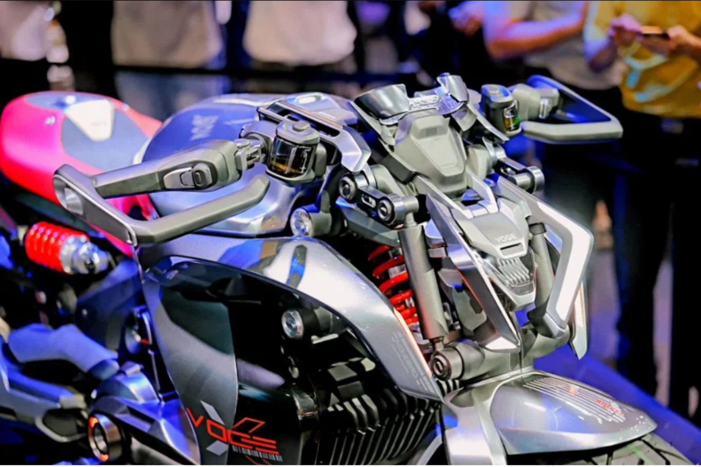 Przedni reflektor LED ma przypominać kły. Nowoczesny motocykl o futurystycznym designie, wyposażony w rozbudowane manetki i elektroniczne wyświetlacze na kierownicy, z widocznymi czerwonymi elementami zawieszenia oraz metalicznym wykończeniem nadwozia.