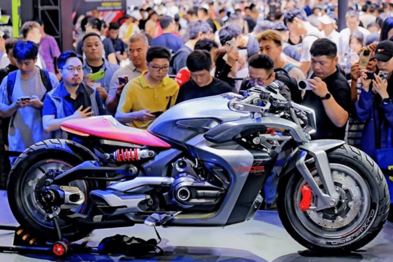 Napęd ma generować łącznie około 100 KM.z Nowoczesny motocykl o agresywnej sylwetce i sportowym designie prezentowany na wystawie, otoczony tłumem zainteresowanych osób fotografujących i oglądających pojazd z bliska.