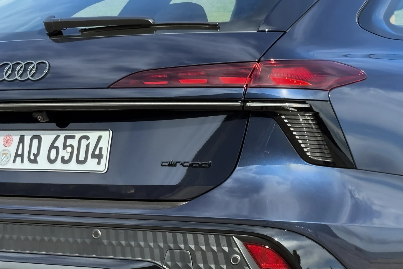 Tylna część niebieskiego samochodu marki Audi z charakterystycznymi tylnymi światłami LED oraz widocznym napisem allroad, poniżej tablica rejestracyjna z numerem AQ 6504.