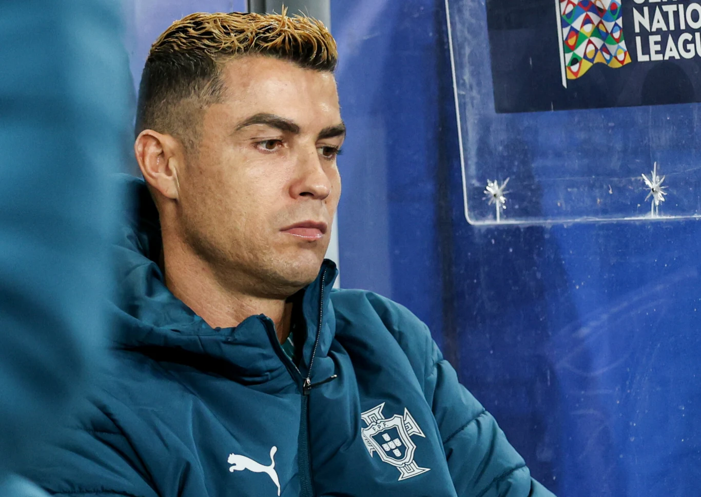 Zawodnik w kurtce sportowej z herbem Portugalii siedzący na ławce rezerwowych podczas meczu piłkarskiego UEFA Nations League.