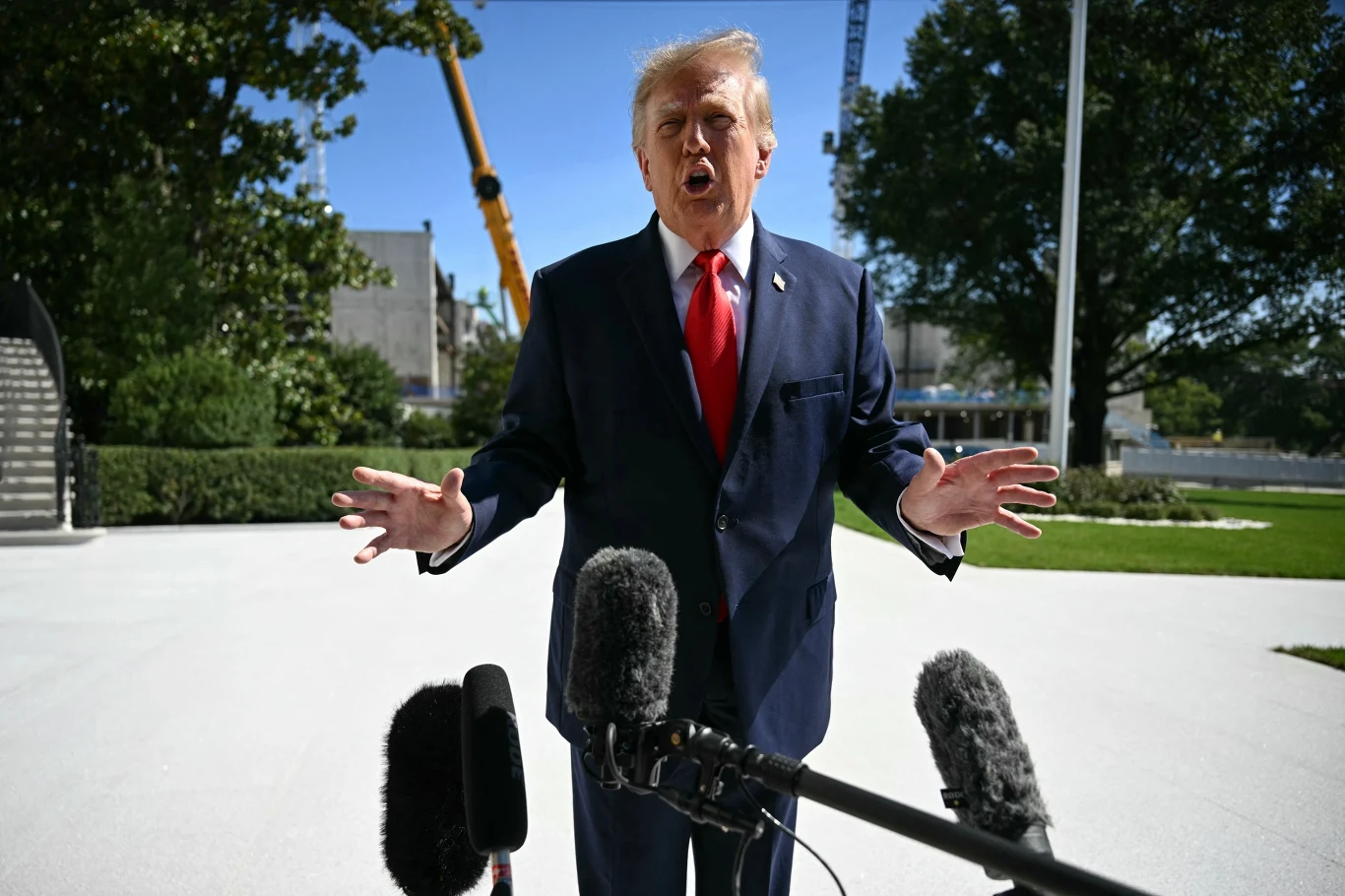 USA nakładają na Iran kolejne sankcje. Na zdj. Donald Trump w czwartek 1 października. Donald Trump w garniturze i czerwonym krawacie przemawia do dziennikarzy w otoczeniu mikrofonów, w tle drzewa i sprzęt budowlany