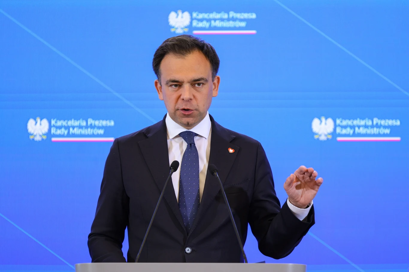 Minister finansów i gospodarki Andrzej Domański Andrzej Domański przemawia przy mównicy na tle ścianki z logo Kancelarii Prezesa Rady Ministrów.
