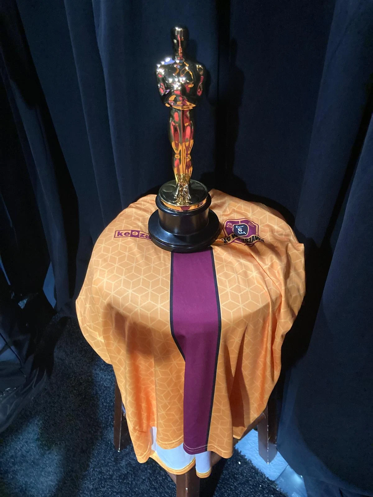 Tarn Willers na historyczną dla siebie galę Oscarów zabrał koszulkę AFC Warszawa. Oto dowód Statuetka Oscara ustawiona na okrągłym stoliku przykrytym pomarańczowo-bordową koszulką sportową z herbem klubu piłkarskiego.