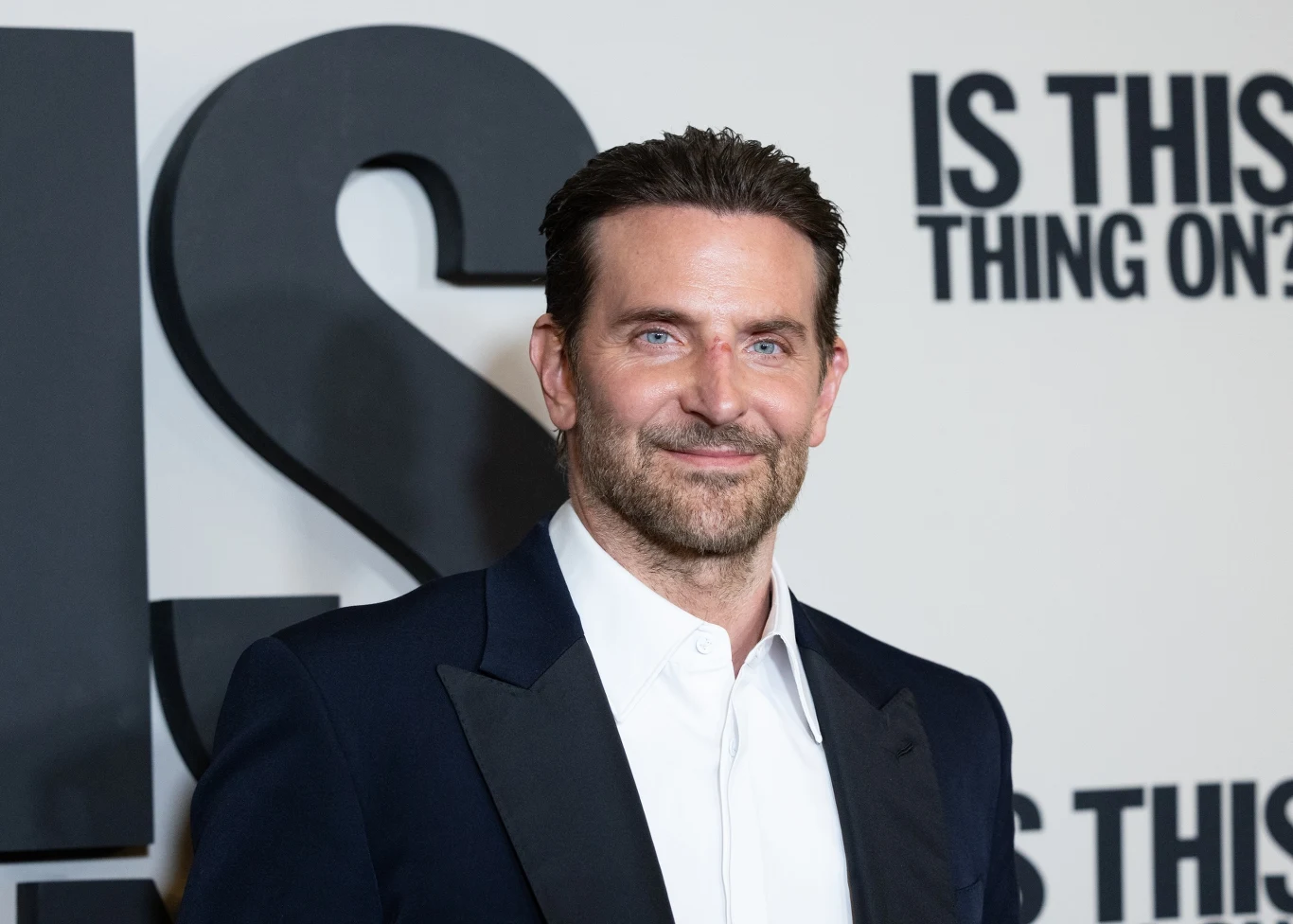 Bradley Cooper w grudniu 2025 roku Bradley Cooper w garniturze i białej koszuli, stojący na tle ściany z czarnymi napisami, grudzień 2025.