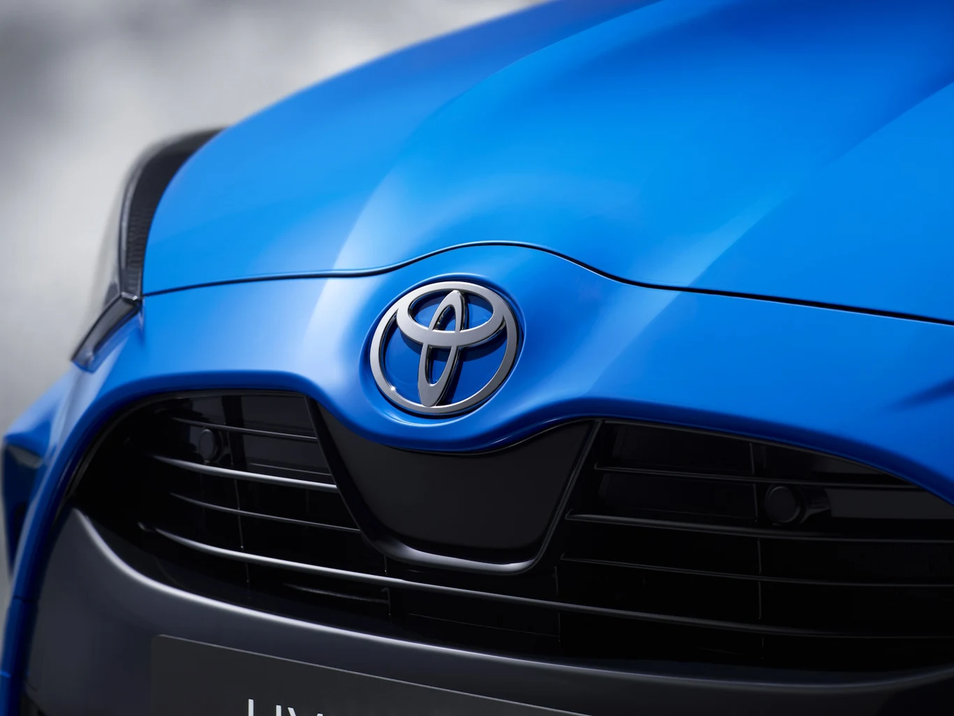 Niebieski przód samochodu Toyota z wyeksponowanym logo marki i czarną atrapą chłodnicy.