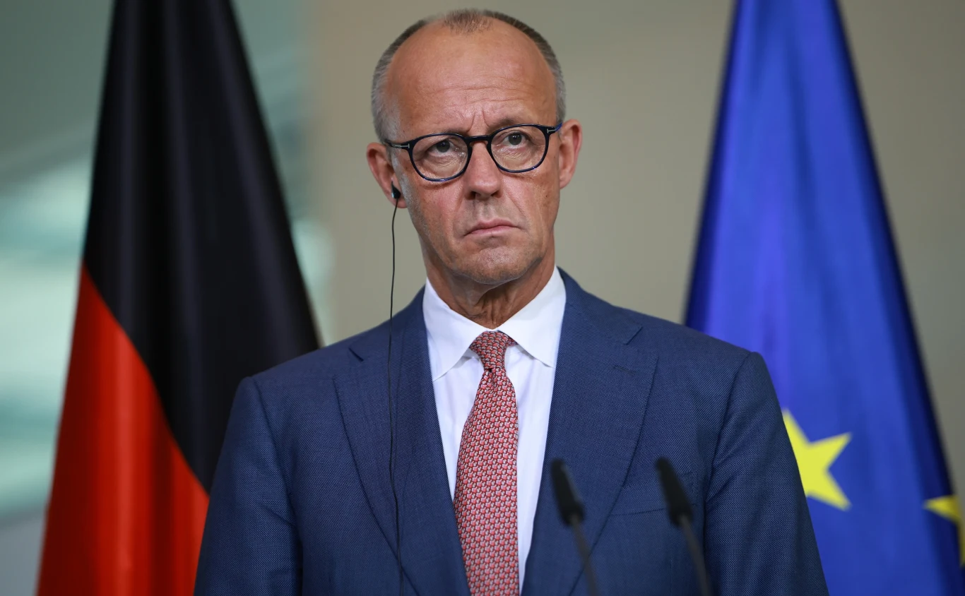 Tylko co dziesiąty Niemiec jest zadowolony z kanclerza Friedricha Merza - wynika z najnowszego sondażu Kanclerz Niemiec Fridrich Merz w garniturze i okularach na tle flag Niemiec i UE.
