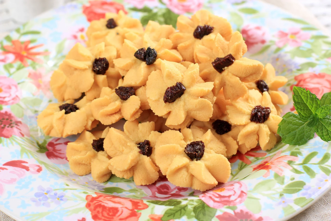 Mocno maślne i kruche ciasteczka z maszynki Ciasteczka z maszynki w kształcie kwiatów z rodzynkami na kolorowym talerzu z motywem kwiatowym.