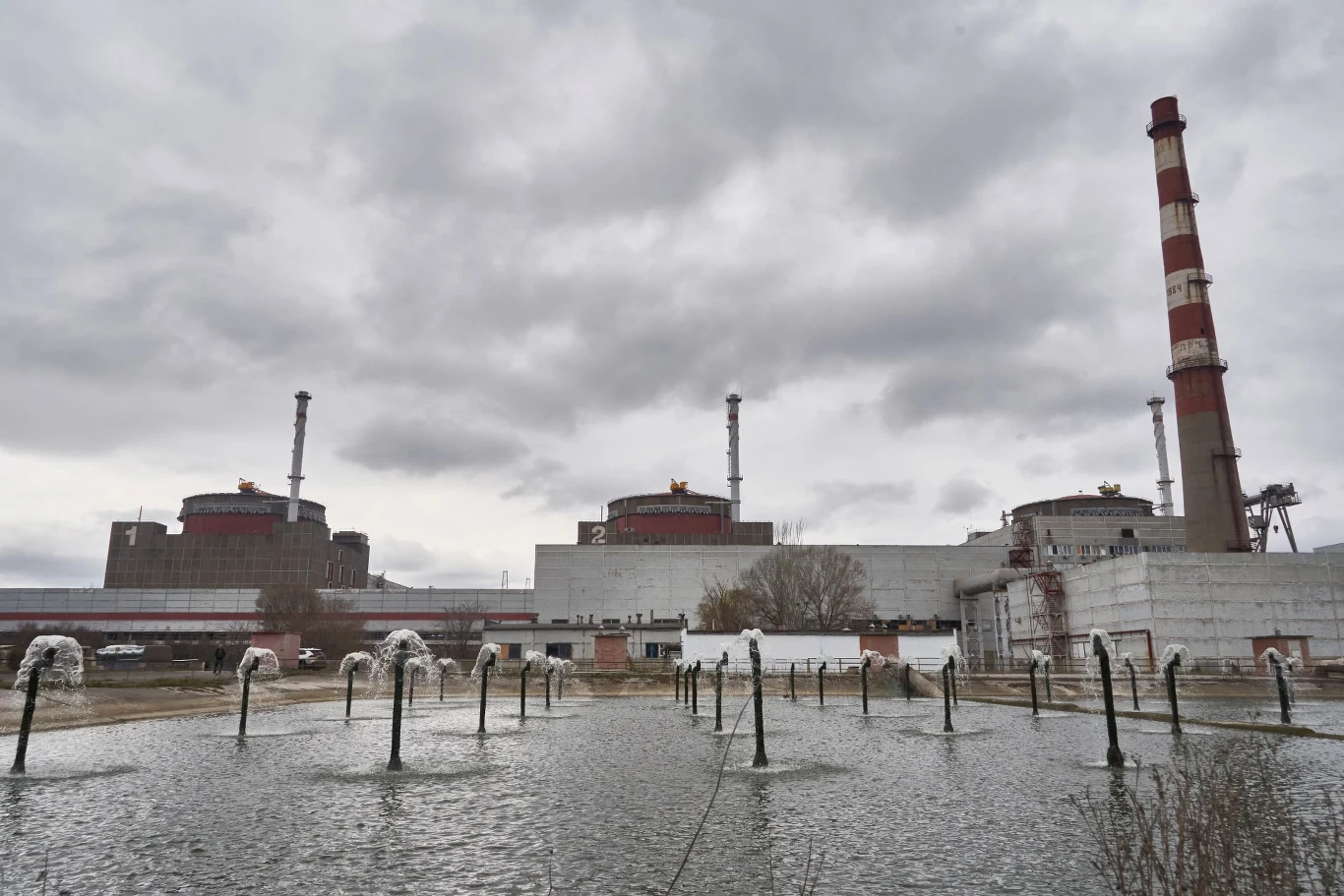 Rosja planuje uderzenie w infrastrukturę krytyczną Ukrainy Kompleks elektrowni jądrowej z trzema reaktorami, wysokim kominem i zbiornikiem wodnym pod pochmurnym niebem.