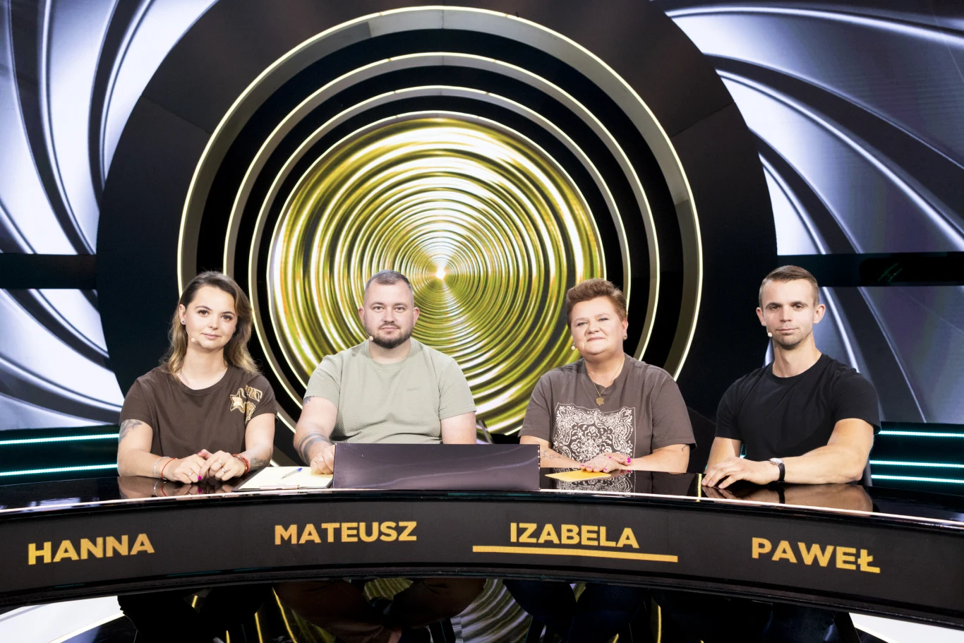 Czworo osób siedzi przy nowoczesnym, podświetlonym stole z wyraźnie widocznymi imionami: Hanna, Mateusz, Izabela, Paweł, na tle graficznej, złotej spirali za nimi.