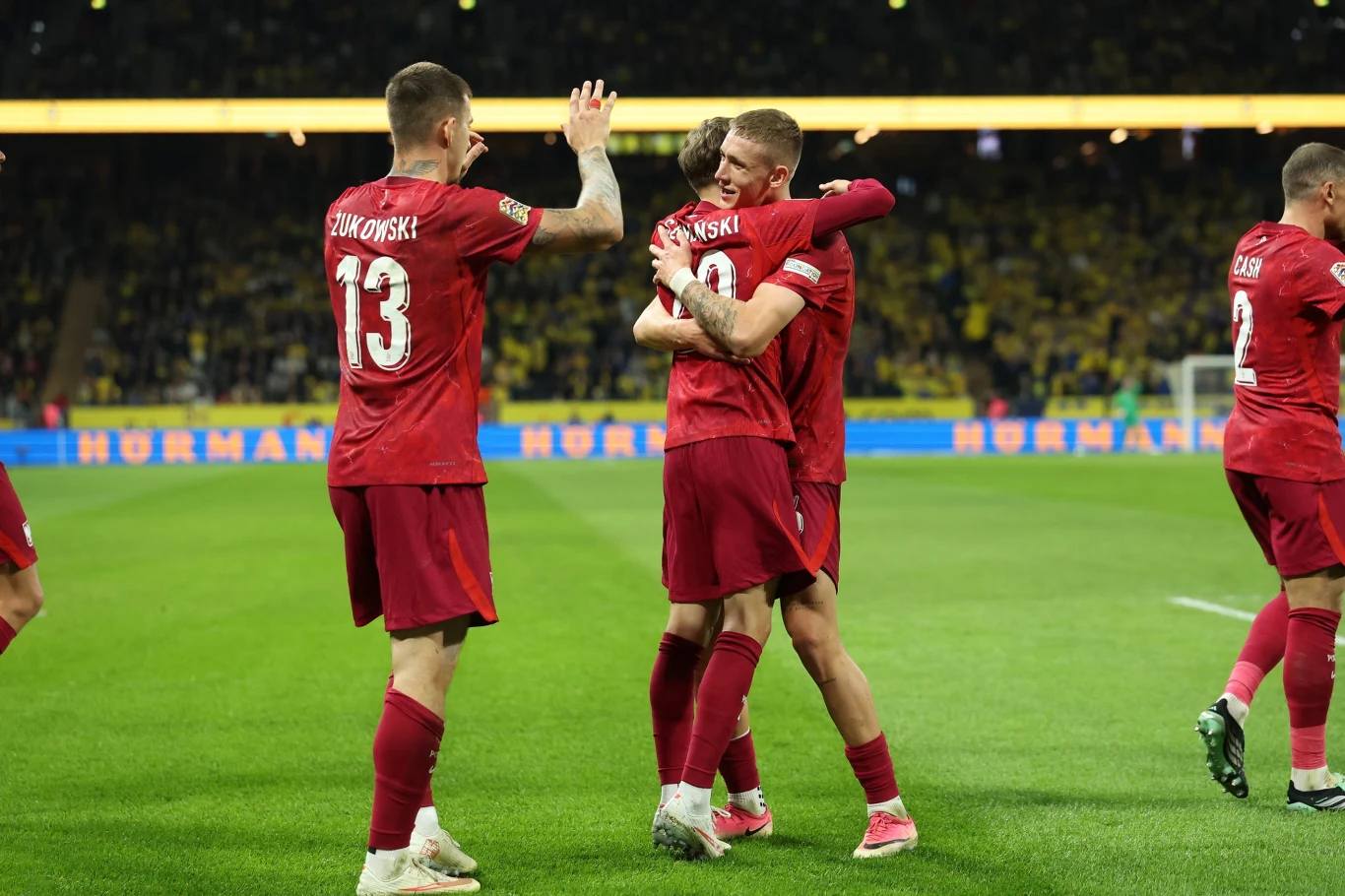 Sebastian Szymański w objęciach Wiktora Nowaka Sebastian Szymański i Wiktor Nowak w czerwonych strojach reprezentacji Polski na murawie stadionu po golu