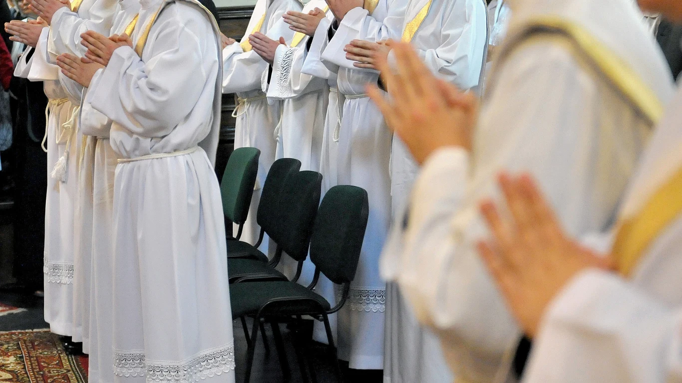 Seminaria szukają ratunku. Odpowiedzią alumni z zagranicy (zdj. ilustracyjne) Grupa alumnów w białych szatach liturgicznych stoi w rzędzie z dłońmi złożonymi do modlitwy.