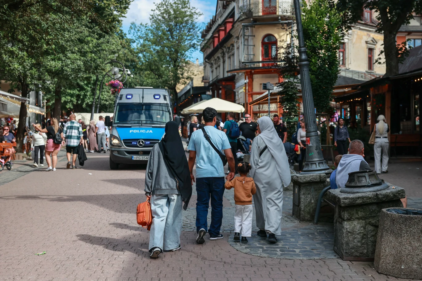Arabscy turyści zaczęli się ostrzegać przed mandatami, jaki dostają od polskiej policji i straży miejskiej Turyści spacerują deptakiem obok policyjnego radiowozu w otoczeniu miejskich zabudowań.