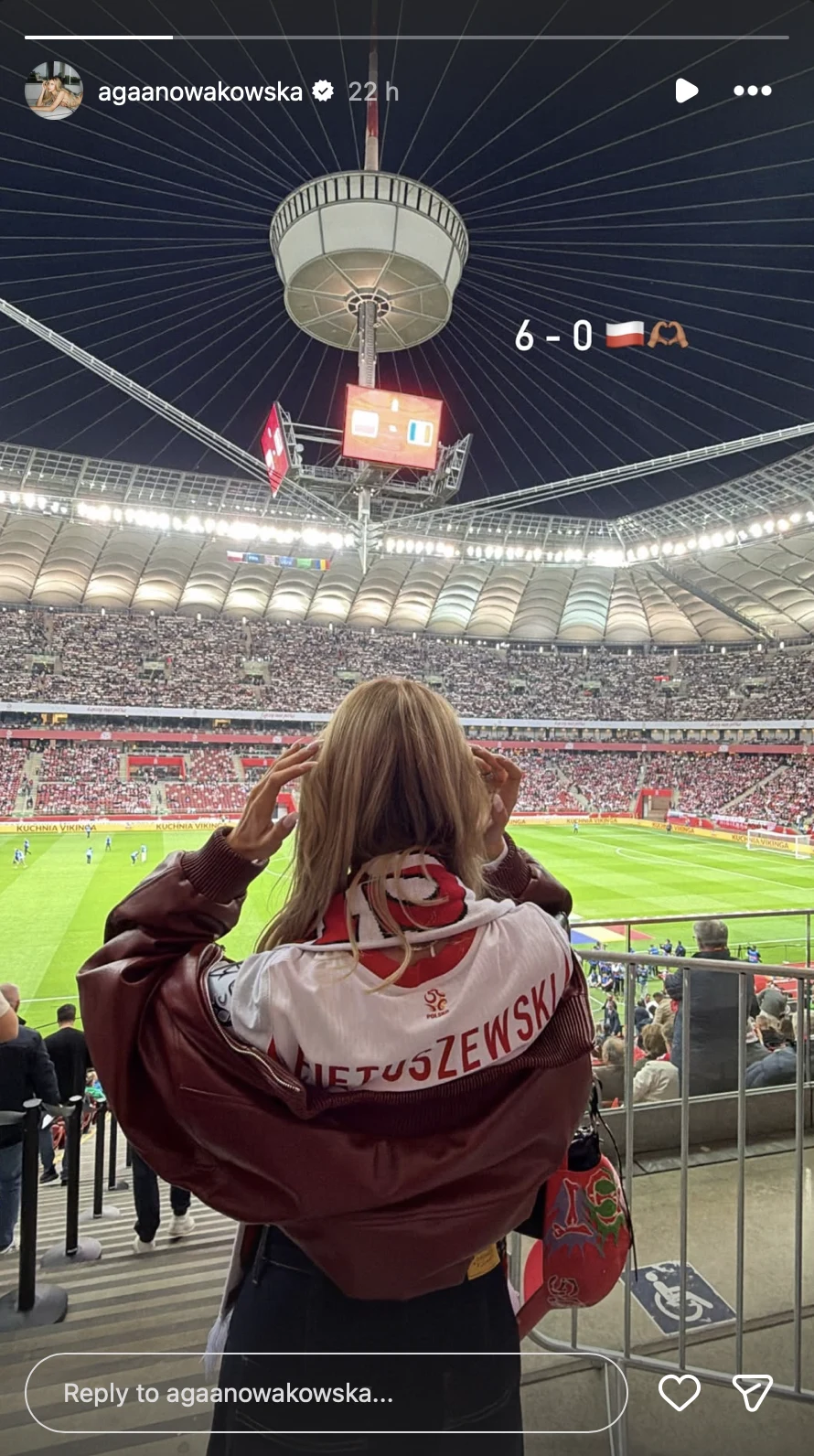 Kibicka ubrana w koszulkę reprezentacji Polski z nazwiskiem Kluśniewski stoi na trybunach Stadionu Narodowego, obserwując rozgrywany mecz piłki nożnej z wynikiem 6:0 widocznym na ekranie stadionowym.