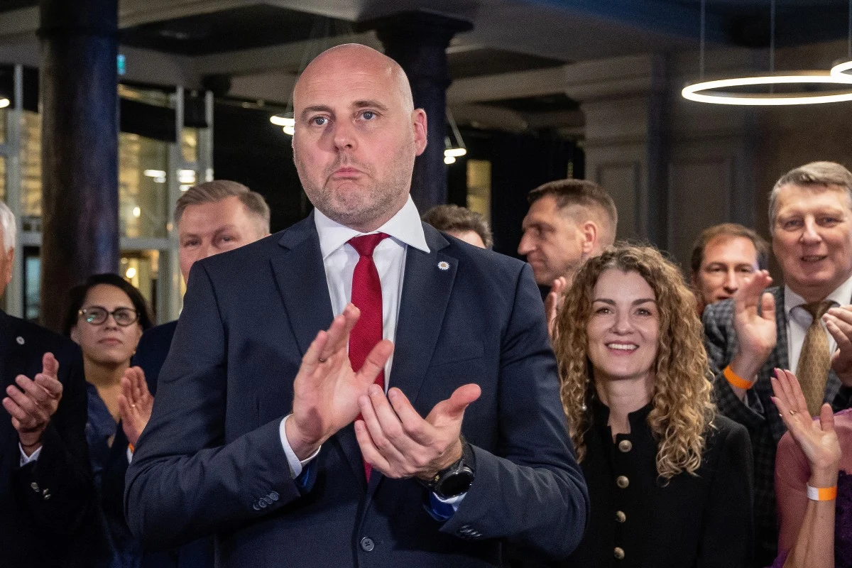 Premier Łotwy Andris Kulbergs reaguje na wstępne wyniki wyborów Premier Łotwy Andris Kulbergs w garniturze bije brawo, obok grupa ludzi także klaszcze na publicznym wydarzeniu.