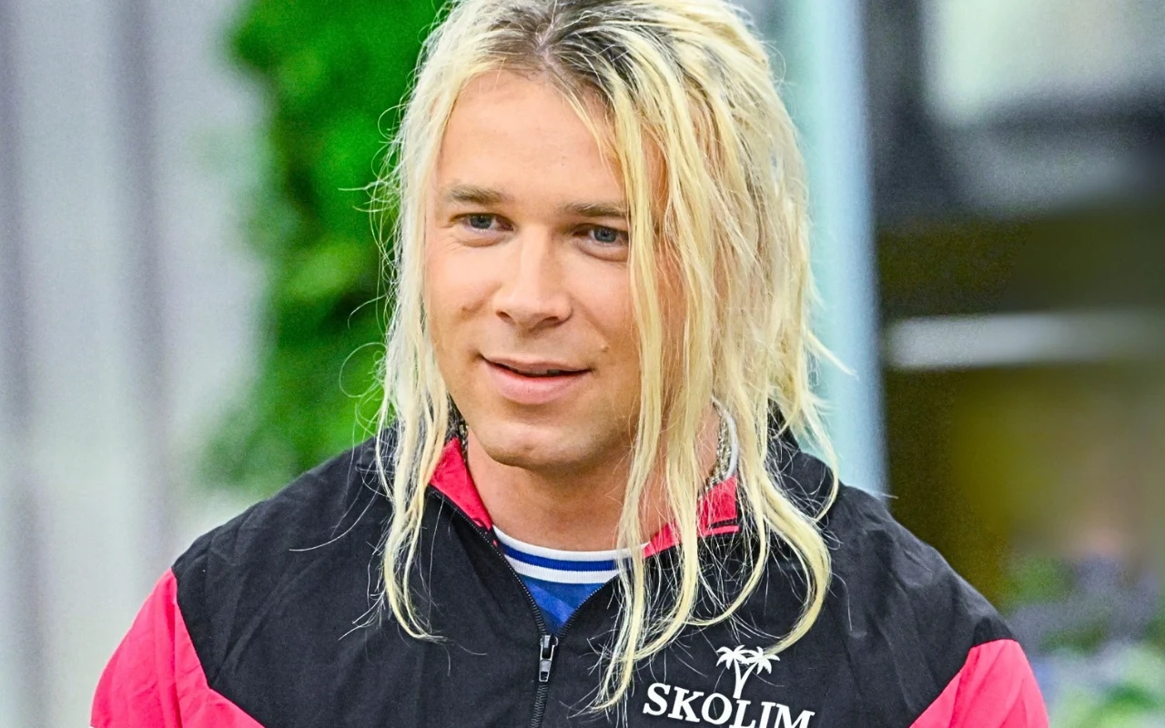 Skolim w "halo tu polsat" Skolim w studiu 'halo tu polsat', młody mężczyzna z długimi blond włosami w czarno-czerwonej kurtce z napisem SKOLIM