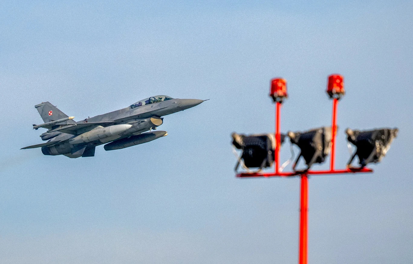 Alert RCB po rosyjskim ataku na Ukrainę. Polska poderwała myśliwce Polski myśliwiec F-16 z szachownicą na stateczniku wznosi się obok czerwonej konstrukcji z reflektorami